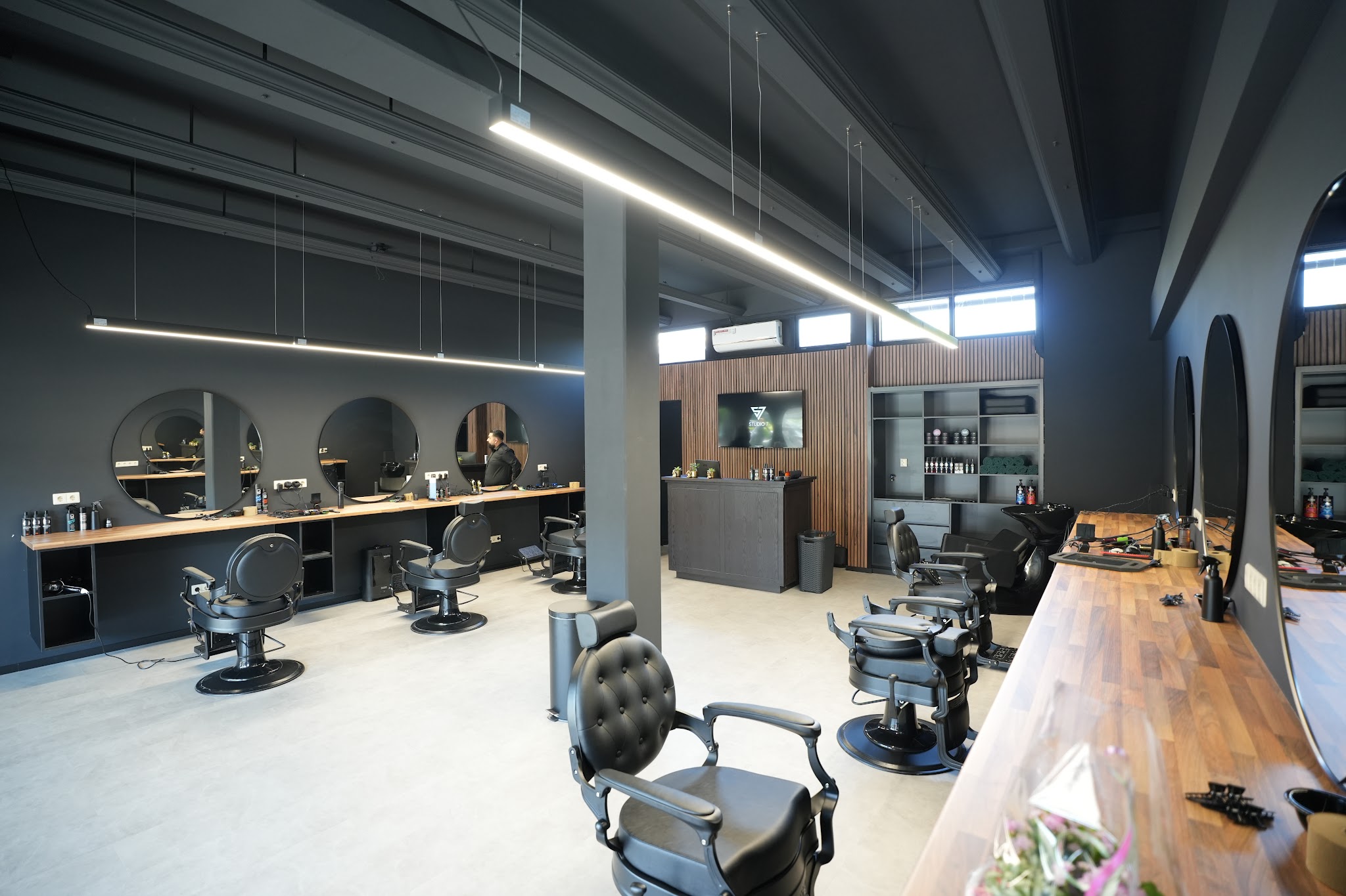 Het interieur van Studio Seven: een rij barberstoelen langs een houten werkblad, zwarte wanden en ledverlichting