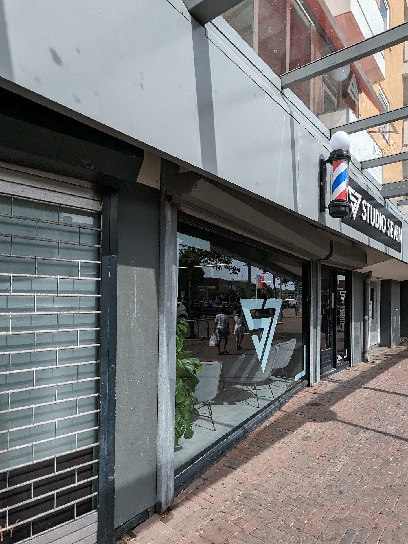 De winkelgalerij aan de Van Hogendorplaan met de gevel van Studio Seven, de barberpaal en het S7-logo op het raam