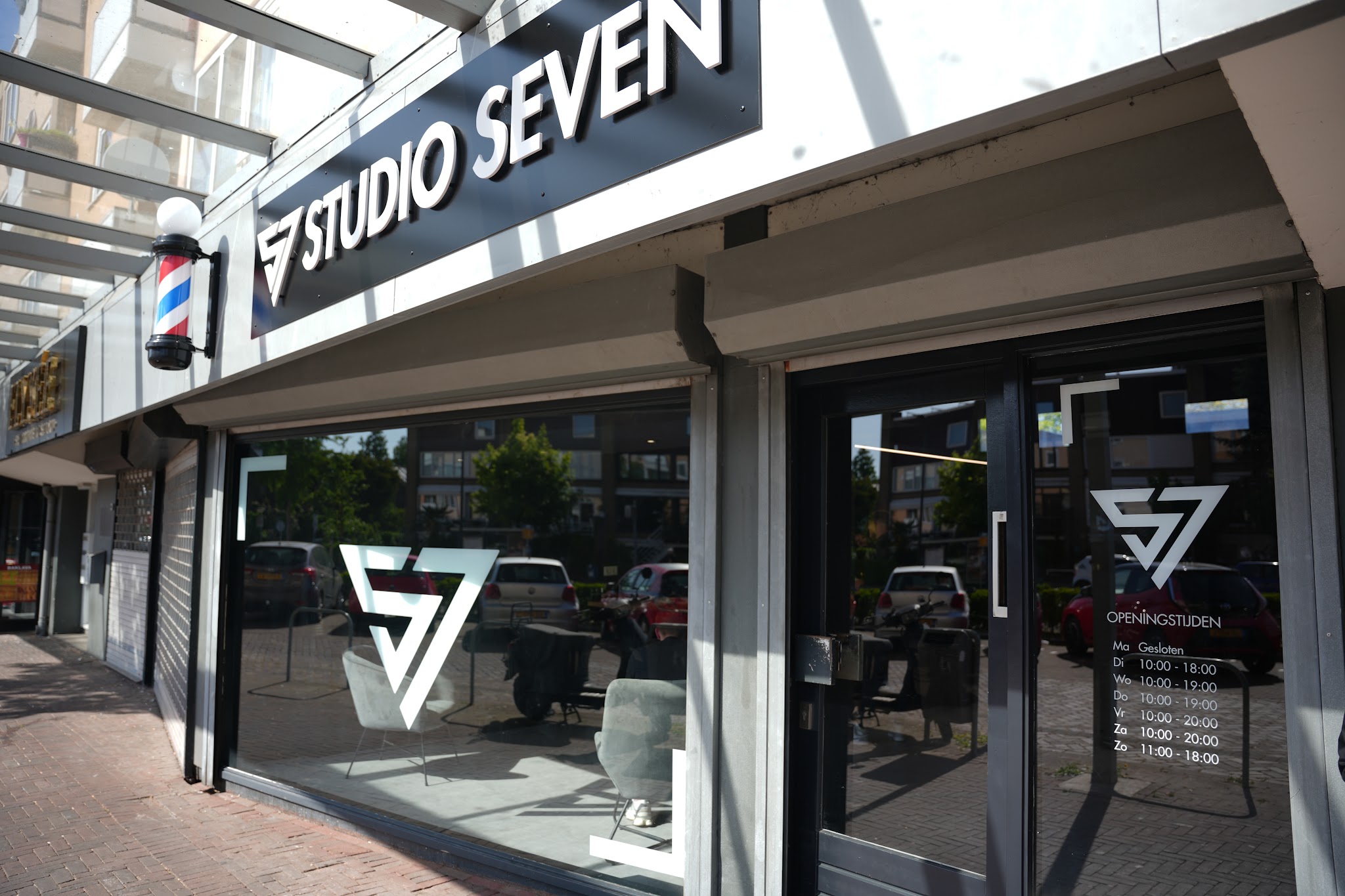 De gevel van Studio Seven met het naambord, de barberpaal en het S7-logo op het raam