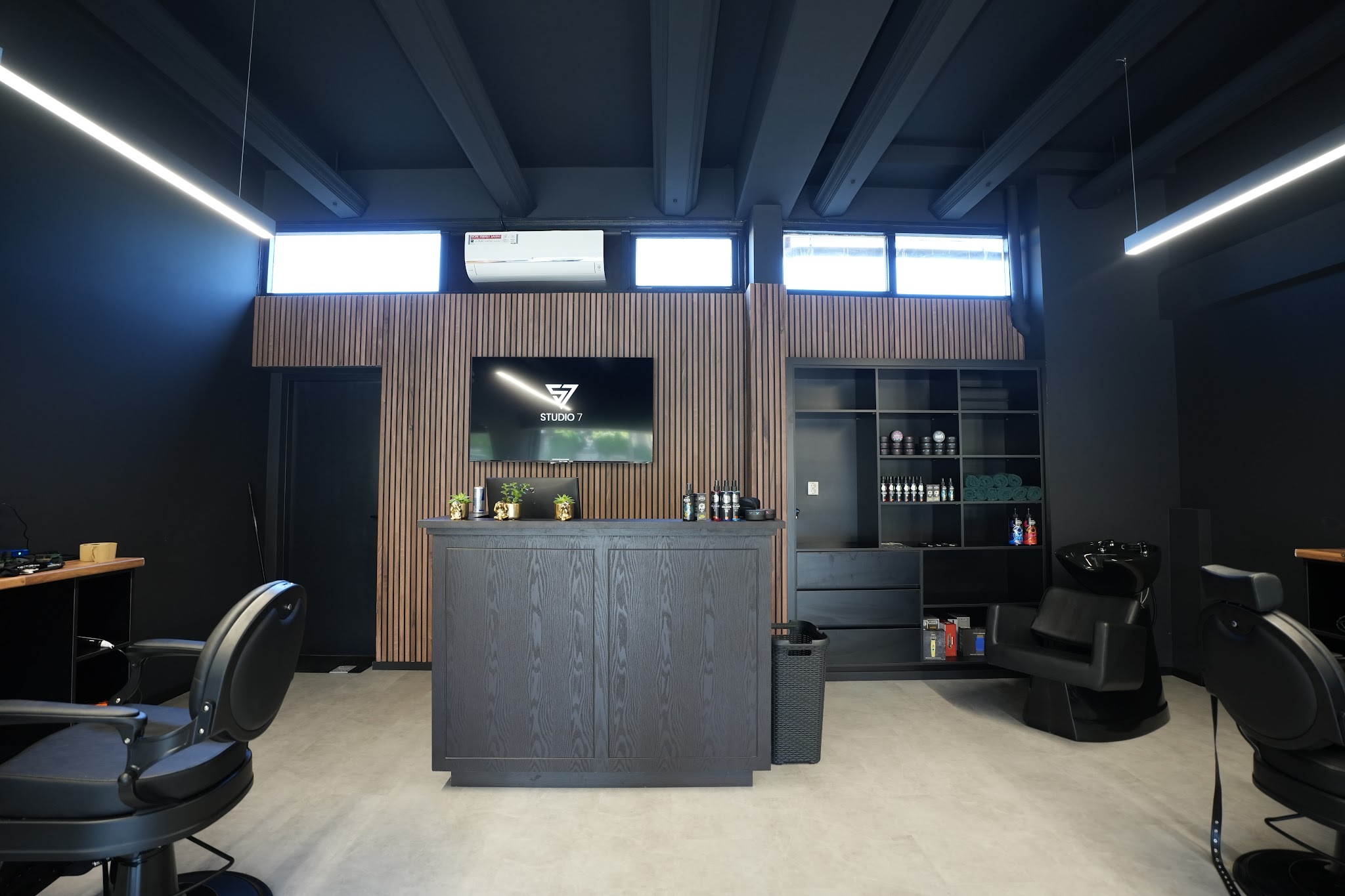 De balie van Studio Seven voor een houten wand, met wasstoelen en een barberstoel